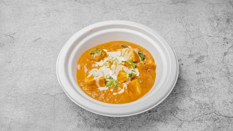 Bowl of creamy tomato curry soup garnished with cream and green herbs on gray background