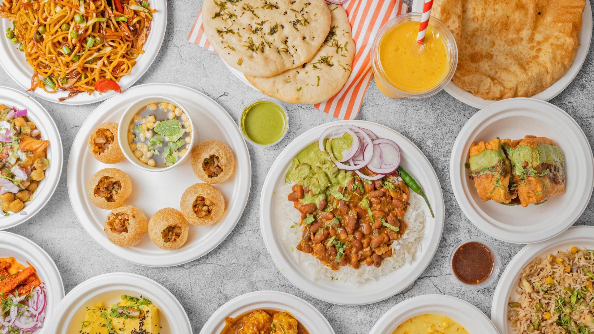 Overhead view of Indian cuisine spread with various dishes including noodles, breads, curries, and small appetizers arranged on white plates