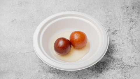 Two red apples in a white bowl with liquid on a gray textured surface