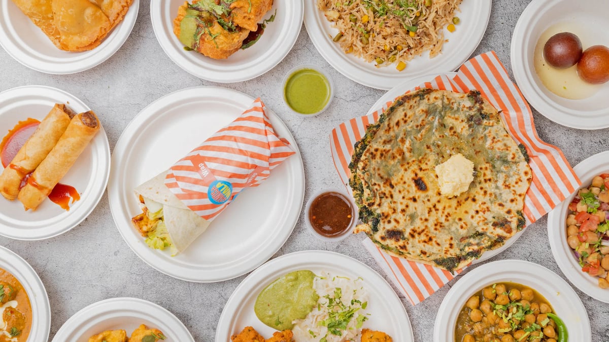Overhead view of a variety of Indian dishes including naan bread, curry, rice, and vegetables arranged on white plates on a gray surface